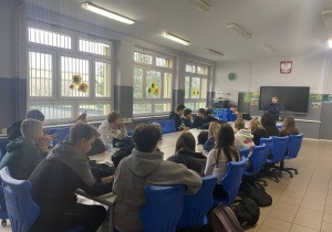 Duża grupa uczniów słucha wykładu pani policjant.