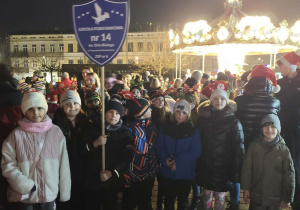 Przedstwaiciele klasy 3a podczas parady Mikołajkowej na Placu Kościuszki, jeden z uczniów trzyma tarczę szkoły.