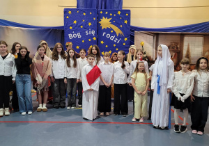 Duża grupa uczniów, aktorów szkolnych jasełek na tle dekoracji.