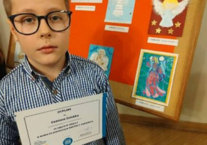 Damian z dyplomem na tle prac plasycznych.