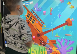 Rozwiązywanie zadań językowych. Chłopiec przed tablica interaktywną.