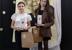 Karlina i Ula z nagrodmi i dyplomami na tle portretu ks. Jana Twardowskiego