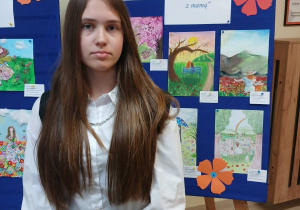 Oliwia stoi przy swojej nagrodzonej pracy plastycznej.
