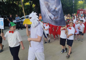 Uczeń w stroju orła prowadi dużą grupe uczniów podczas tomaszowskiej parady