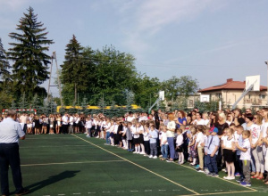 Na boisku szkolnym galowo ubrani uczniowie są witani przez dyrektora szkoły.