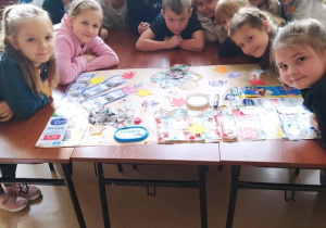 Grupa uczniów pochylona nad stolikiem na którym leży wielki plakat. Do plakatu przyczepione są naklejki z wyrobów mlecznychgRUPA UCZNIÓW POCHYLONA NAD STOLIKIEM NA KTÓRYM LEŻY WIELKI PLAKAT. dO PLAKATU PRZYCZEPIONE SĄ NAKLEJKI Z WYROBÓW MLECZNYCH.