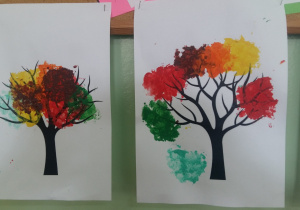 Dwie prace plastyczne przedstawiające kolorowe jesienne drzewa na białym tle wykonane farbami.