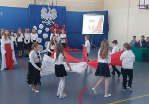Akademia z okazji Święta Odzyskania Niepodległości. Uczniowie ustawieni w kole ze splecionymi na kształt gwiazdy czerwonymi i białymi szalami w rękach.