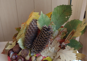 Jesienny kapelusz z papieru ozdobiony suszonymi liśćmi kasztanami i szyszkami.