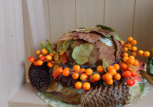 Jesienny kapelusz ozdobiony suszonymi liśćmi jarzębiną i szyszkami.