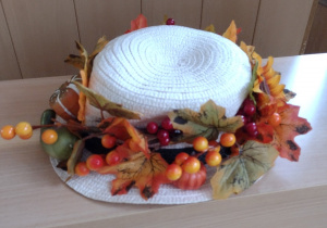 Biały kapelusz ozdobiony jesiennymi liśćmi i jarzębiną.