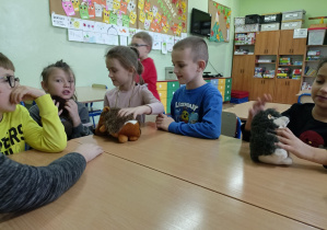 Uczniowie uczęszczający do świetlicy szkolnej siedzą przy ławkach i bawią się pluszowymi jeżykami.