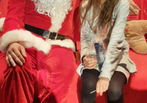 Uśmiechnięta dziewczynka siedzi na czerwonej kanapie w towarzystwie Świętego Mikołaja.