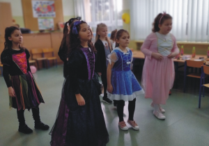 Sześć dziewczynek przebranych za księżniczki stoi w dwóch szeregach w tle okna klasy.