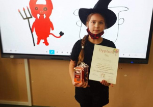 Dziewczynka przebrana za czarownicę na tle tablicy interaktywnej. Na tablicy namalowany czerwony diabełek.