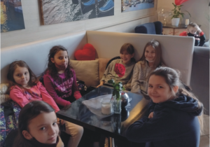 Przy stoliku siedzi sześć dziewczynek które jedzą desery. W tle baloniki i ściana z widokiem Wenecji.