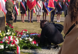 Moment złożenia kwiatów przed pomnikiem. W tle stoją poczty sztandarowe z różnych szkół oraz warta honorowa wojska polskiego.