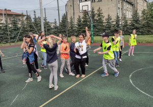 Boisko szkolne. Na boisku stoją dziewczynki i chłopcy przygotowujący się do rozgrywek.