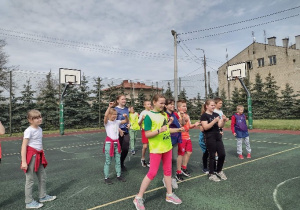 Boisko szkolne. Na boisku stoją dziewczynki i chłopcy przygotowujący się do rozgrywek.