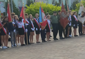 W szeregu stoją poczty sztandarowe z tomaszowskich szkół . W tle widoczna kamienica.