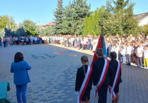 Poczet sztandarowu ustawiony tyłem. W tle uczniowie SP 14 ustawieni na placu szkolnym.