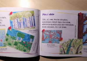 Otwarta książka z kolorowymi ilustracjami leży na jasnym blacie.