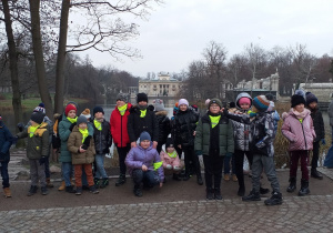 Duża grupa dzieci stoi na pierwszym planie . W tle budynek, drzewa i woda.