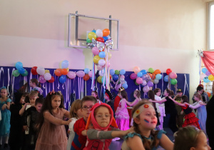 Duża grupa uczniów tanczy w kole. W tle sala ubrana balonami i serpentynami
