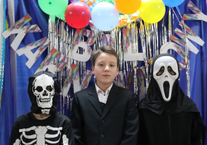 Trzech chłopców pozuje na tle granatowej ścianki ozdobionej lametą i kolorowymi balonami.