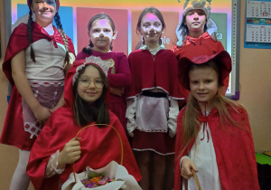 6 dziewczynek przebranych za Czerwone Kapturki stoi na tle tablicy interaktywnej.