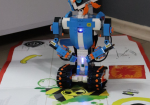 Na bialej planszy stoi robot skonstruowany z klocków lego.