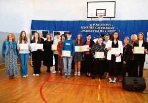 Na niebieskim tle stoi duża grupa uczniów i nauczycieli.