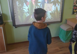 Chłopiec stoi tyłem przed tablicą internaktywną. Na tablicy wyświetla się animowany obraz.