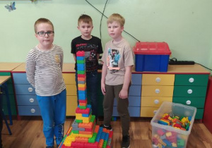 Chłopcy budują wieżę z kolorowych klocków. W tle szafa i kolorowe komody.