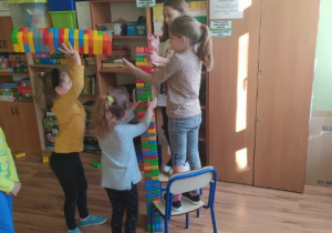 Dziewczęta budują wieżę z kolorowych klocków. W tle stoją szafa.