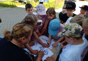 Grupa dzieci pochyla się nad stolikiem. Na stoliku leżą rozłożone kartki.