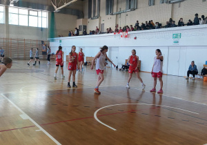 Sala gimnastyczna. Dziewczęta w czerwonych i białych strojach grają mecz. W tle trybuny i widownia.