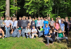 Duża grupa uczniów pozuje do zdjęcia na tle lasu.