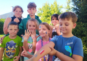 Grupa dziewcząt i chłopców prezentuje kropki namalowane na twarzy i rękach. W tle drzewa.