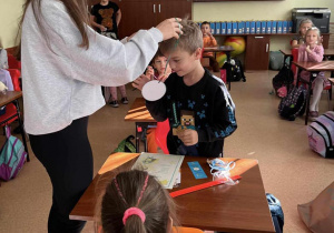 Dziewczyna zawiesza na szyi chłopaka medal za zwycięstwo w konkursie. pozostali uczniowie obserwują dekorację.