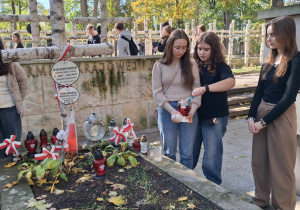 Trzy uczennice odpalają znicz przy grobie Aleksandra Kamińskiego na Powązkach w Warszawie