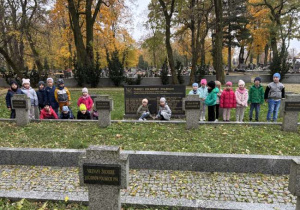 Dzieci na cmentarzu zapalają znicze na grobach żołnierzy