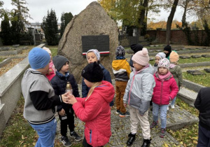 Dzieci na cmentarzu zapalają znicze na grobach żołnierzy