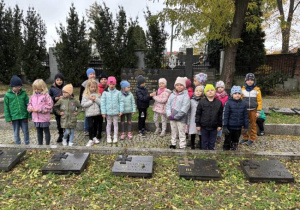 Dzieci na cmentarzu zapalają znicze na grobach żołnierzy