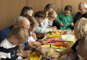 Seniorzy wraz z dziećmi wykonują pracę plastyczną "Słońce serdeczności"