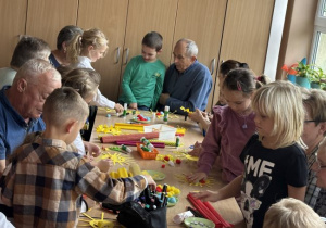 Seniorzy wraz z dziećmi wykonują pracę plastyczną "Słońce serdeczności"