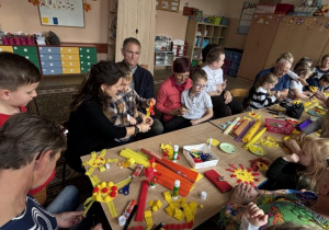 Seniorzy wraz z dziećmi wykonują pracę plastyczną "Słońce serdeczności"