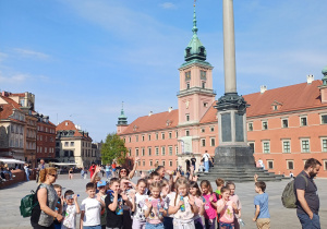 Grup uczniów klasy pierwszej na Placu Zamkowym w Warszawie. Za nimi Kolumna Zygmunta