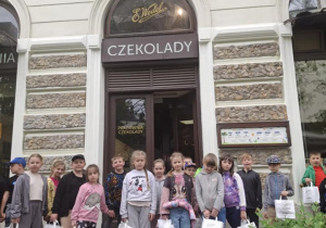 Duża grupa zadowolonych uczniów przed fabryką czekolady.