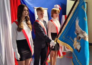 Poczet sztandarowy wraz ze sztandarem na tle biało czerwonej flagi.